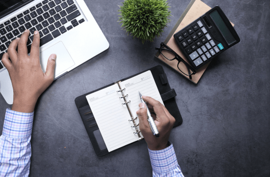 Person writing in planner beside laptop and calculator to represent operational planning Cerity Global's - Ongoing Support Services